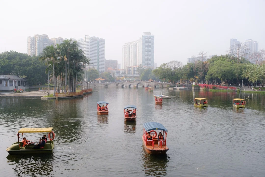Boats sail across a lake in front of buildings.